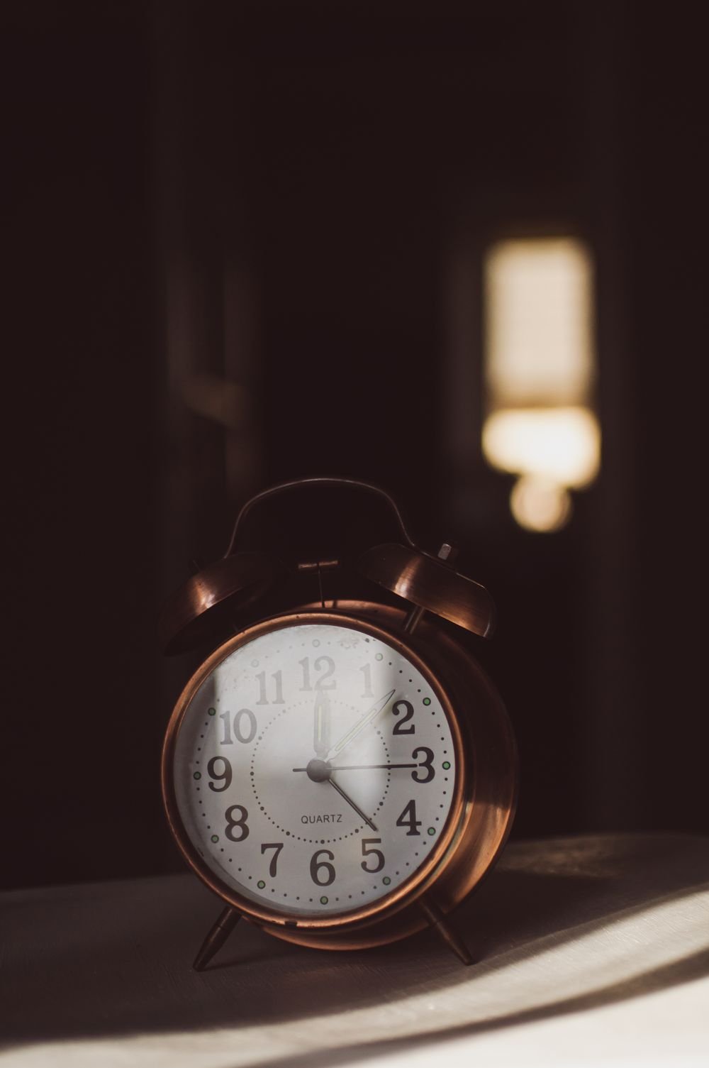 A vintage copper alarm clock catching warm morning light on a bedside table