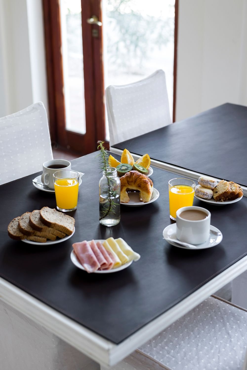 A set breakfast table with a cup of coffee, orange juice, sliced bread and a croissant in morning light