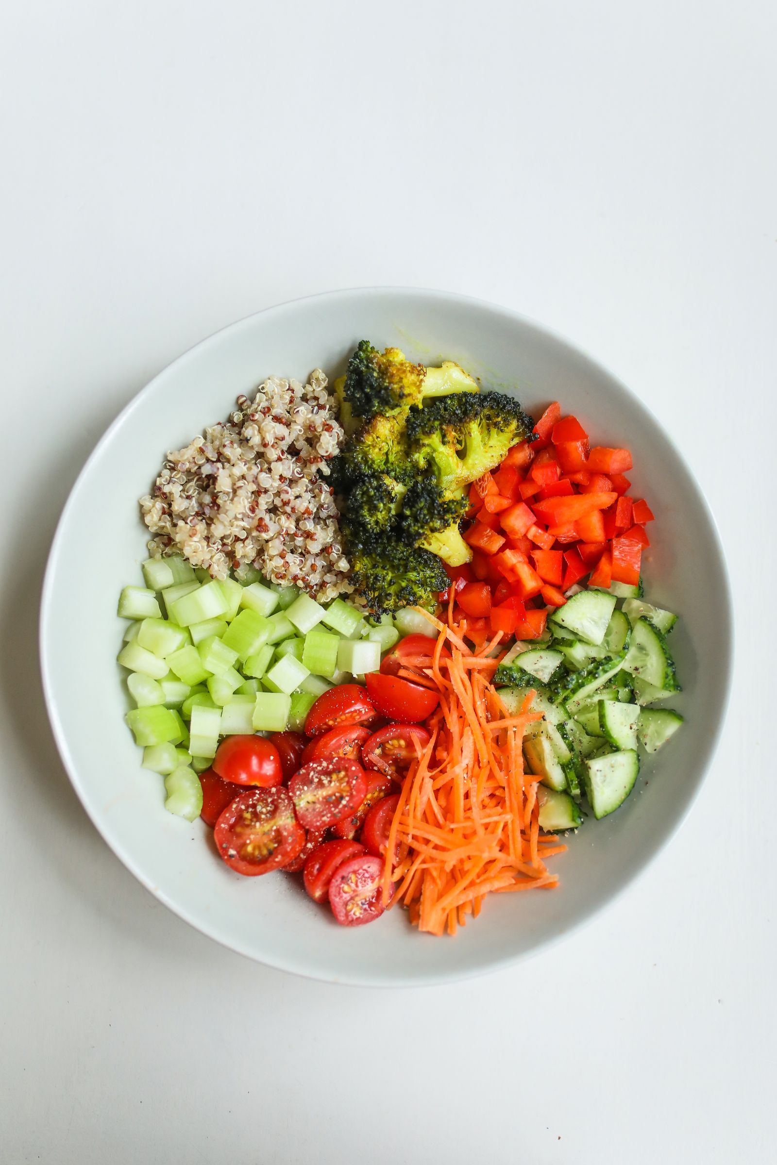 A bowl divided into quinoa, roasted broccoli, red pepper, celery, cherry tomatoes, carrot and cucumber