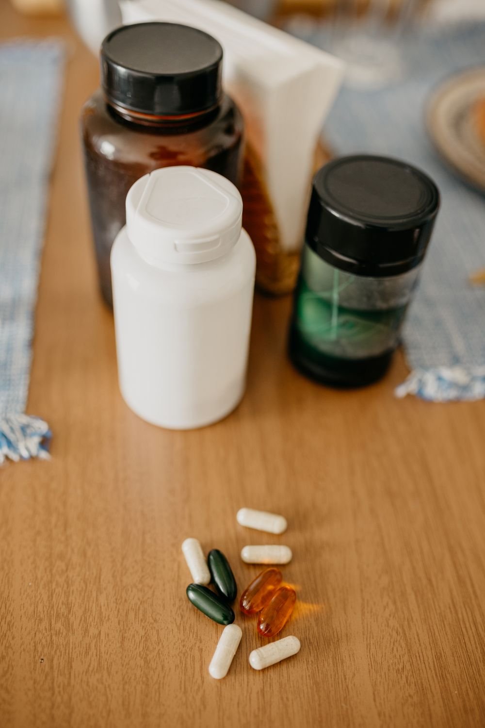 Three unlabeled supplement bottles and loose capsules scattered on a wooden table
