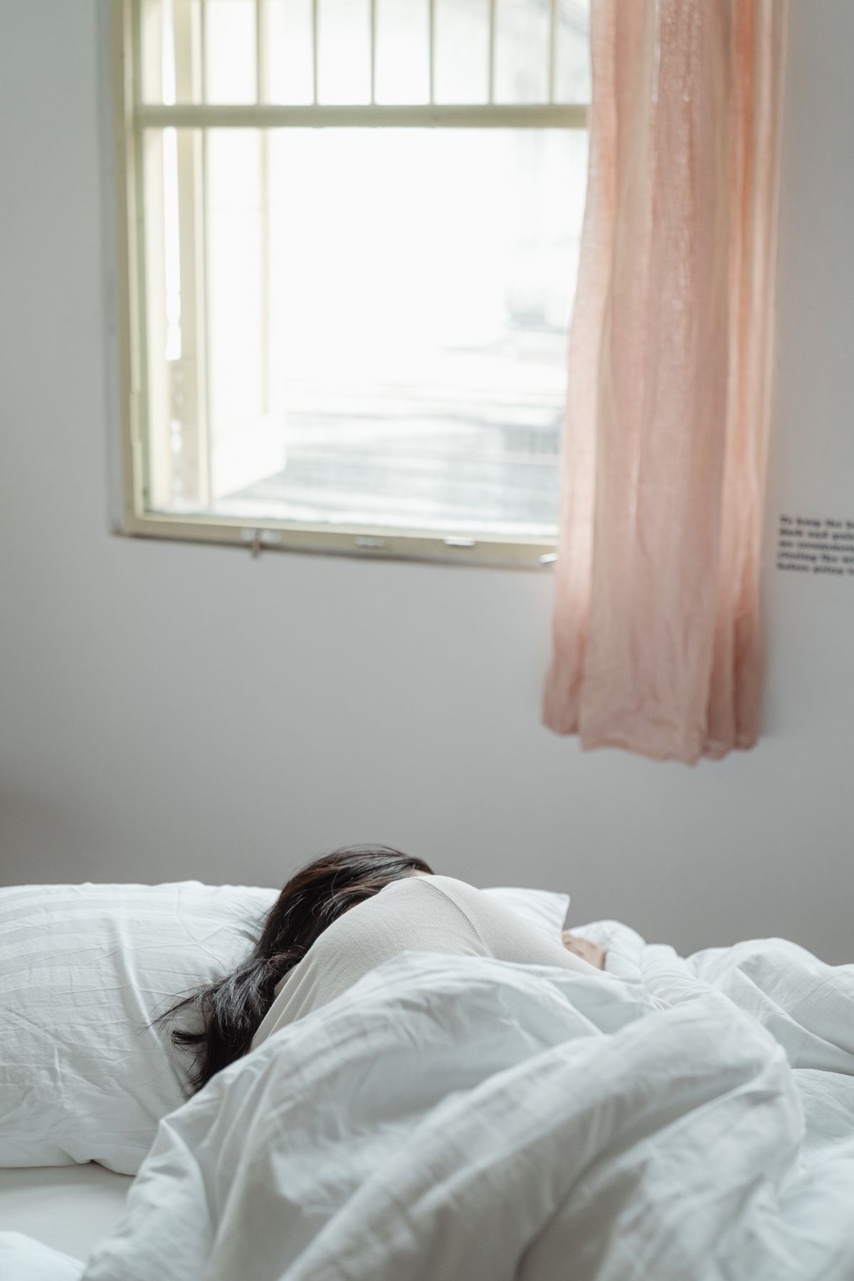 A person sleeping peacefully under white bedding in a bright bedroom with soft natural light