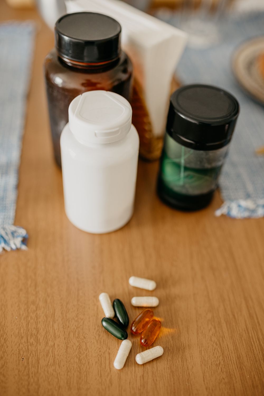 Three supplement bottles on a wooden kitchen table with assorted capsules spilled in front of them