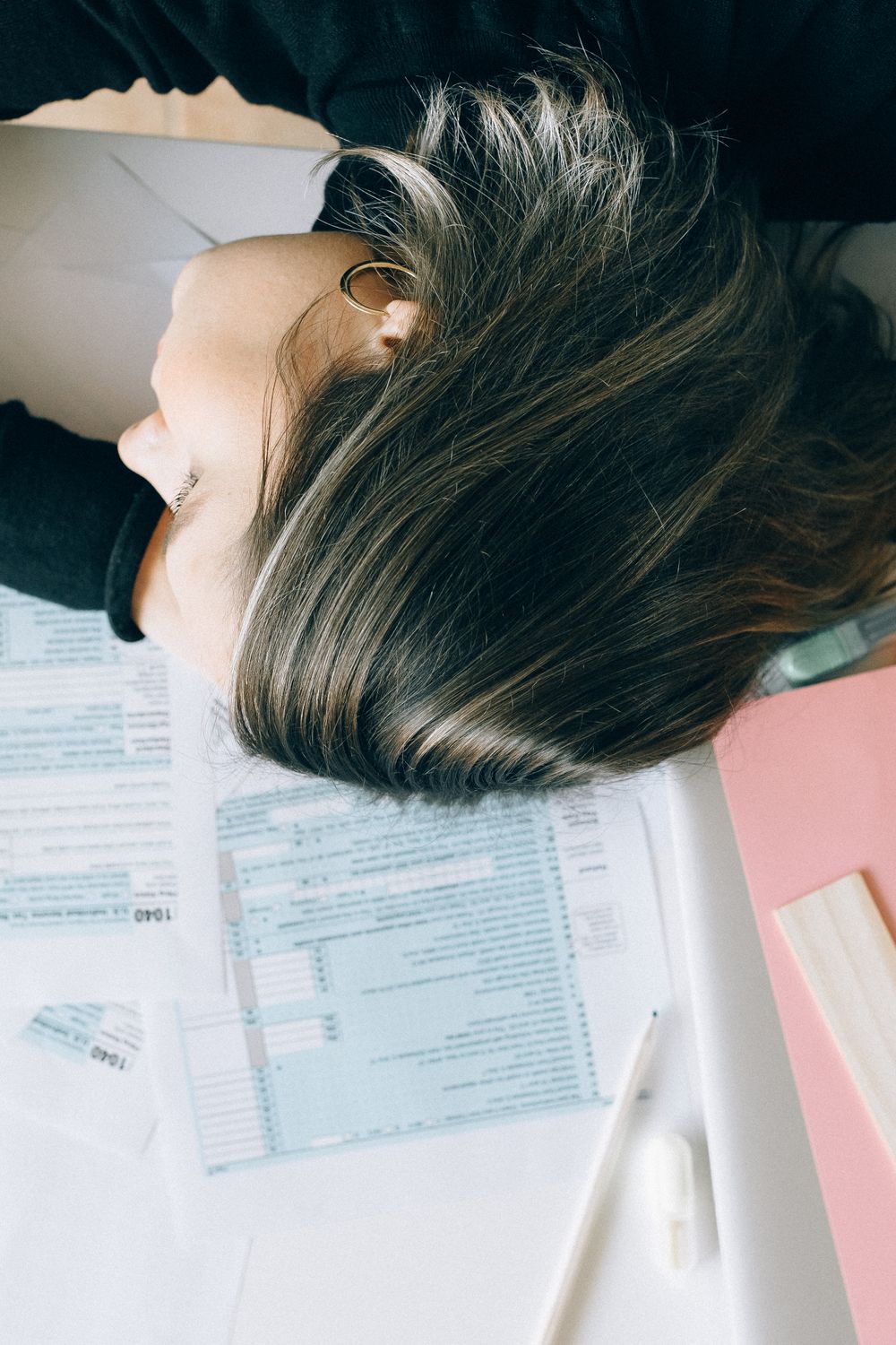 A woman resting her head down on a desk covered in paperwork, exhausted in the middle of the workday
